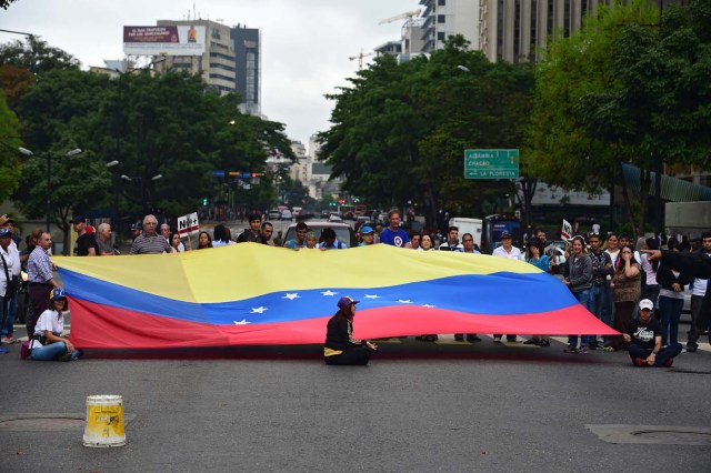 Demonstrators display a Venezuelan national flag as they block a street during a protest against Venezuelan President Nicolas Maduro in Caracas, on May 2, 2017. Venezuelan President Nicolas Maduro called for a new constitution Monday as he fights to quell a crisis that has led to more than a month of protests against him and deadly street violence. The opposition slammed the tactic as a "coup d'etat" and urged protesters to "block the streets" from Tuesday. It said it was organizing a "mega protest" for Wednesday. / AFP PHOTO / RONALDO SCHEMIDT