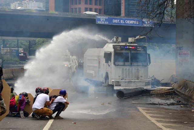 Demonstrators are sprayed by a riot police water cannon during clashes within a protest against Venezuelan President Nicolas Maduro, on May 3, 2017. Venezuela's angry opposition rallied Wednesday vowing huge street protests against President Nicolas Maduro's plan to rewrite the constitution and accusing him of dodging elections to cling to power despite deadly unrest. / AFP PHOTO / RONALDO SCHEMIDT