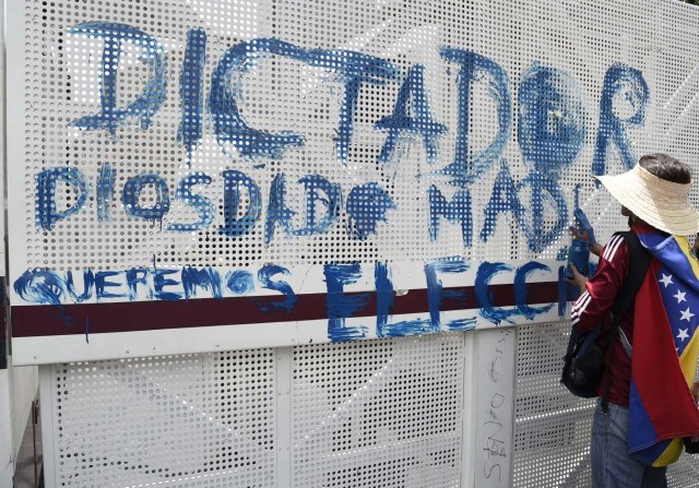 A Venezuelan opposition activist paints a graffiti on a fence during a women's march aimed to keep pressure on President Nicolas Maduro, whose authority is being increasingly challenged by protests and deadly unrest, in Caracas on May 6, 2017. The death toll since April, when the protests intensified after Maduro's administration and the courts stepped up efforts to undermine the opposition, is at least 36 according to prosecutors. / AFP PHOTO / JUAN BARRETO