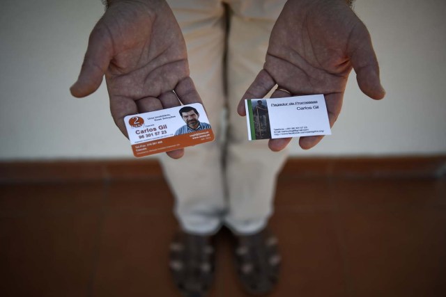 Carlos Gil poses for a photo holding business cards listing his occupation as a "payer-off of promises" (R) and "real estate agent"(L) at his house backyard in Cascais, outskirts of Lisbon, on April 7, 2017.  Carlos Gil is a payer-off of promises, at least that is the way the Roman Catholic refers to himself. But he is more commonly known as a rent-a-pilgrim. This 52-year-old Portuguese national takes on pilgrimages by proxy (in the name of others), especially Catholics unable to fulfil the journey because of sickness or too busy or lazy to undertake the week-long spiritual walk to the central Portuguese town of Fatima. He can be hired for an average cost of 2,500 euros. / AFP PHOTO / PATRICIA DE MELO MOREIRA / TO GO WITH AFP STORY BY BRIGITTE HAGEMANN