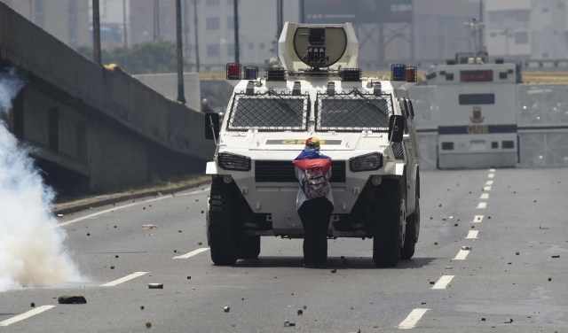 (FILES) This file photo taken on April 19, 2017 shows a demonstrator standing in front of an armoured vehicle of the riot police during a rally against Venezuelan President Nicolas Maduro, in Caracas on April 19, 2017. "It hurt me to see how they were firing at the kids," she said later, referring to the rubber bullets and tear gas used by police against protesters. / AFP PHOTO / Juan BARRETO