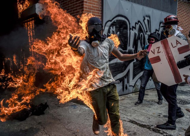 (FILES) This file photo taken on May 03, 2017 shows a demonstrator catching fire after the gas tank of a police motorbike exploded during clashes in a protest against Venezuelan President Nicolas Maduro, in Caracas on May 3, 2017. From his hospital bed where he lay in bandages with burns on 70 percent of his body, Victor Salazar sent a video urging protesters: "Get out into the street, not for me but for Venezuela." / AFP PHOTO / JUAN BARRETO