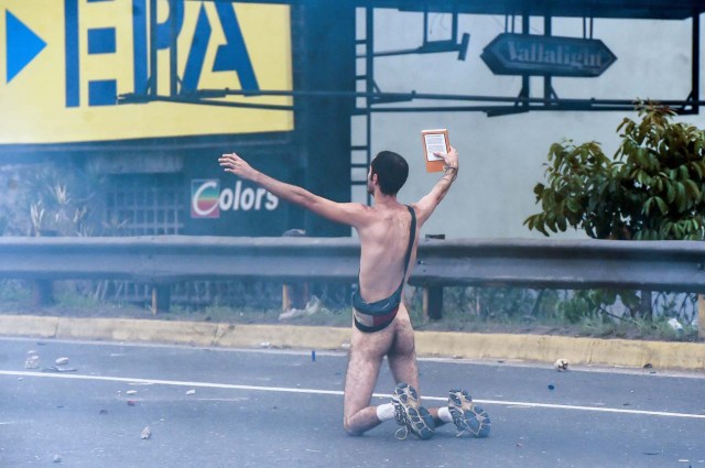 EDITORS NOTE: Graphic content / (FILES) This file photo taken on April 20, 2017 shows a naked demonstrator taking part in a protest against Venezuelan President Nicolas Maduro, in Caracas on April 20, 2017. Wearing nothing but white sports shoes and socks, a money belt and an anguished expression, Hans Wuerich, 27, raised a bible in his skinny hand as he stood on top of a police armored car on April 20. "I'm not some flower-power hippy," he told AFP later. "But I do believe that peaceful protest does more harm to the government than violence. I stunned them."  / AFP PHOTO / JUAN BARRETO