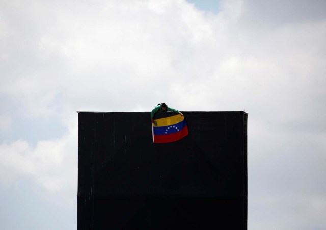An opposition supporter hang a national flag on top of an advertising structure while rallying against President Nicolas Maduro in Caracas, Venezuela, May 20, 2017. REUTERS/Carlos Garcia Rawlins