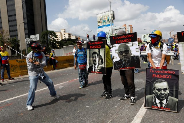 Demonstrators carry signs with images of President Nicolas Maduro (L) and politician Jorge Rodriguez and judge Maikol Moreno (R) that reads "your real enemy" while rallying against President Nicolas Maduro in Caracas, Venezuela, May 27, 2017. REUTERS/Carlos Garcia Rawlins