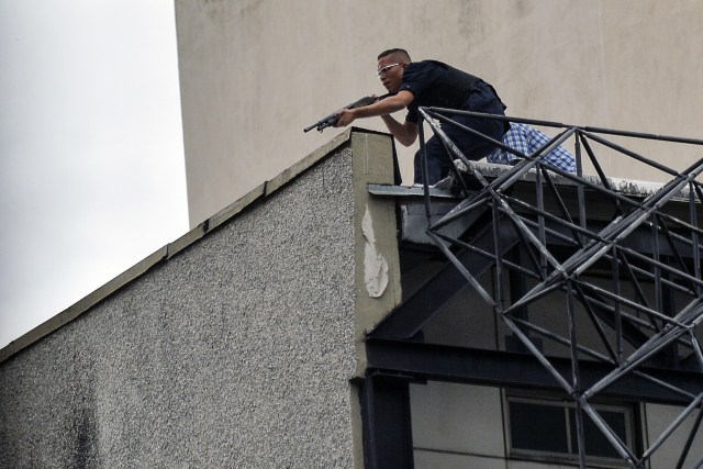 A man aims his weapon at demonstrators as they attack the administration headquarters of the Supreme Justice Court during riots following a protests against President Nicolas Maduro's government in Caracas, Venezuela, on June 7, 2017. The head of the Venezuelan military, General Vladimir Padrino Lopez, who is also President Nicolas Maduro's defence minister, is warning his troops not to commit "atrocities" against protesters demonstrating in the country's deadly political crisis. Tuesday's warning came after more than two months of violent clashes between protesters and security forces. The opposition and a press rights group say security forces have run over, attacked and robbed protesters and journalists. / AFP PHOTO / LUIS ROBAYO