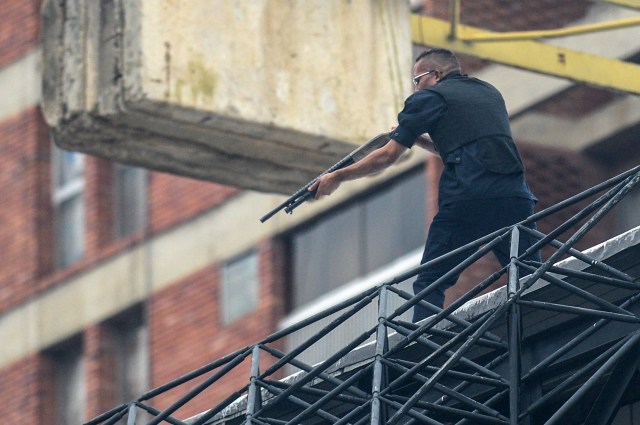 A man aims his weapon at demonstrators as they attack the administration headquarters of the Supreme Justice Court during riots following a protests against President Nicolas Maduro's government in Caracas, Venezuela, on June 7, 2017. The head of the Venezuelan military, General Vladimir Padrino Lopez, who is also President Nicolas Maduro's defence minister, is warning his troops not to commit "atrocities" against protesters demonstrating in the country's deadly political crisis. Tuesday's warning came after more than two months of violent clashes between protesters and security forces. The opposition and a press rights group say security forces have run over, attacked and robbed protesters and journalists. / AFP PHOTO / FEDERICO PARRA