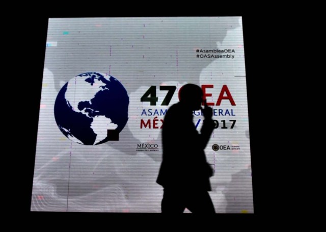 A man passes by a screen displaying the logo of the 47th General Assembly of the Organization of American States (OAS) in the Mexican resort city of Cancun, on June 18, 2017. Foreign ministers from the OAS discuss taking action on the crisis in Venezuela -- a meeting that has infuriated President Nicolas Maduro's government -- ahead of the regional group's general assembly, which runs from Monday through Wednesday. / AFP PHOTO / Pedro PARDO
