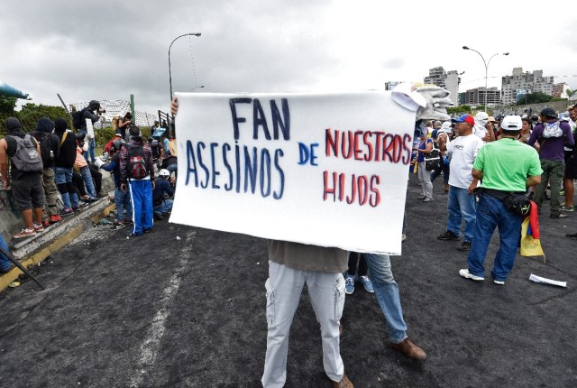 An opposition activist holds a placard reading "FAN (Venezuelan Armed Forces) Murderers of Our Children" during a demonstration against the government of Venezuelan President Nicolas Maduro in Caracas on June 24, 2017, in front of the Francisco de Miranda air force base near the place where a young man was shot dead by police during an anti-government rally two days ago. A political and economic crisis in the oil-producing country has spawned often violent demonstrations by protesters demanding Maduro's resignation and new elections. The unrest has left 75 people dead since April 1. / AFP PHOTO / Juan BARRETO