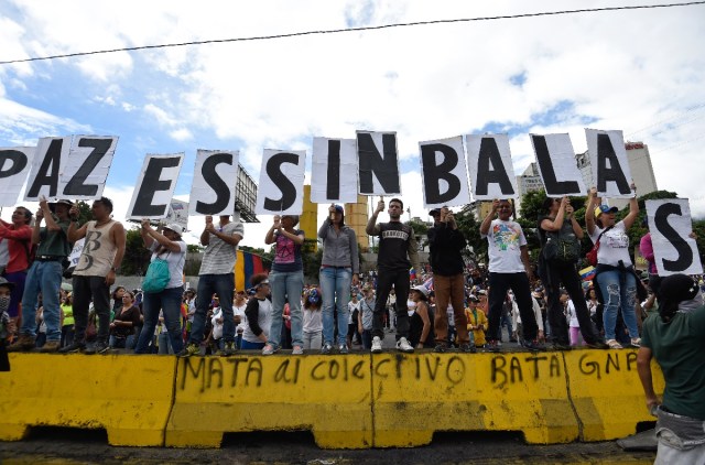 Opposition activists form the sentence "Peace is Without Bullets" during a demonstration against the government of Venezuelan President Nicolas Maduro in Caracas on June 24, 2017, in front of the Francisco de Miranda air force base near the place where a young man was shot dead by police during an anti-government rally two days ago. A political and economic crisis in the oil-producing country has spawned often violent demonstrations by protesters demanding Maduro's resignation and new elections. The unrest has left 75 people dead since April 1. / AFP PHOTO / Juan BARRETO