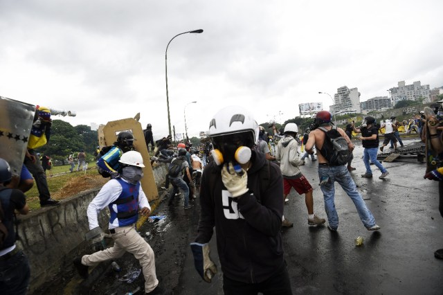 Opposition activists run during clashes with the police at the Francisco de Miranda air force base during a demonstration against the government of Venezuelan President Nicolas Maduro in Caracas on June 24, 2017, near the place where a young man was shot dead by police during an anti-government rally two days ago. A political and economic crisis in the oil-producing country has spawned often violent demonstrations by protesters demanding Maduro's resignation and new elections. The unrest has left 75 people dead since April 1. / AFP PHOTO / JUAN BARRETO