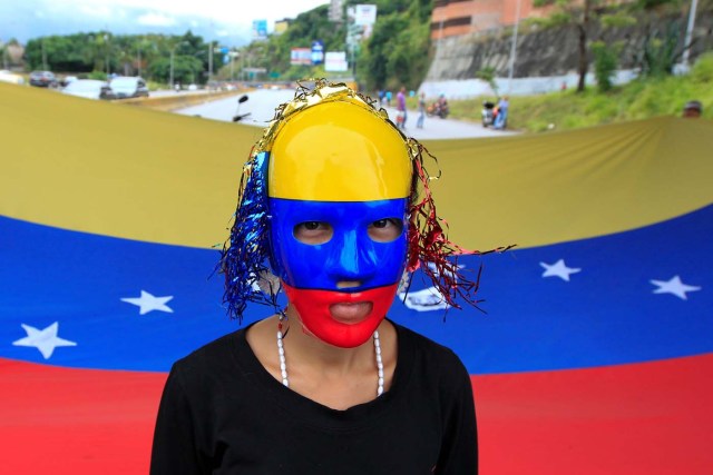 A demonstrator stands in front of a national flag as she blocks a main street with others, during a protests against Venezuelan President Nicolas Maduro's government in Caracas, Venezuela June 14, 2017. REUTERS/Christian Veron
