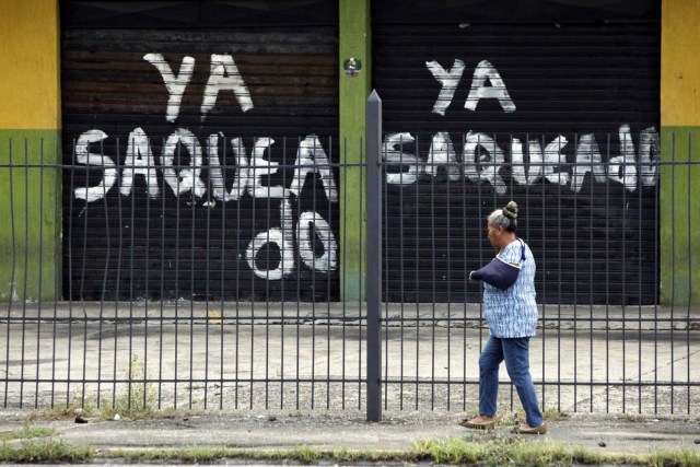 A woman walks past the gates of a shop that read, "Already looted" in Barinas, Venezuela June 12, 2017. Picture taken June 12, 2017. REUTERS/Carlos Eduardo Ramirez