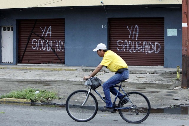 A man rides a bicycle in front of the gates of a shop that read, "Already looted" in Barinas, Venezuela June 12, 2017. Picture taken June 12, 2017. REUTERS/Carlos Eduardo Ramirez