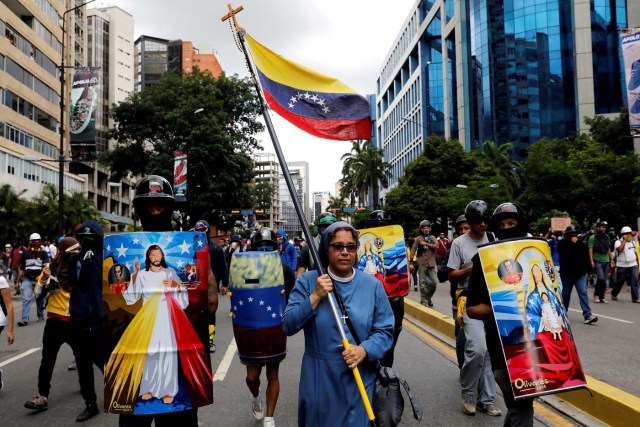 FILE PHOTO: A nun carries Venezuelan flag next to demonstrators carrying homemade shields with religious images, during a rally against Venezuelan President Nicolas Maduro's government in Caracas, Venezuela June 7, 2017. Picture taken June 7, 2017. REUTERS/Carlos Garcia Rawlins/File Photo