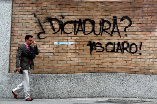 A pedestrian holds a tear gas mask as he walks past a graffiti that reads "Dictatorship? You know!" during a rally against Venezuelan President Nicolas Maduro's government in Caracas, Venezuela June 22, 2017..  REUTERS/Christian Veron