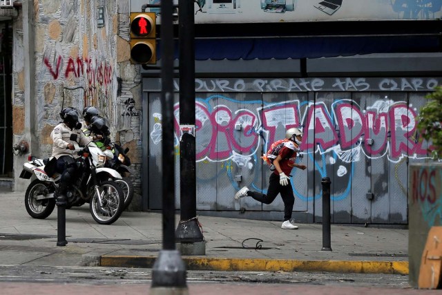 A demonstrator runs away from riot security forces while rallying against Venezuela's President Nicolas Maduro's government in Caracas, Venezuela June 29, 2017. The graffiti reads "Dictatorship". REUTERS/Ivan Alvarado
