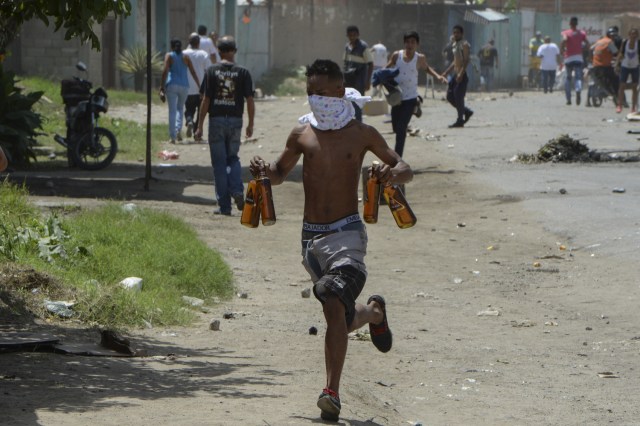 Un joven corre con botellas de alcohol robadas después de saquear un supermercado en Maracay, estado de Aragua, Venezuela, el 27 de junio de 2017. / AFP PHOTO / Federico Parra