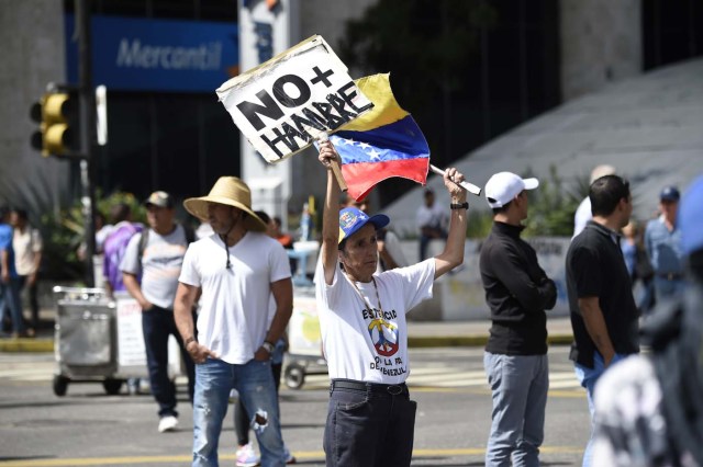An opposition activist demonstrating against the government of Venezuelan President Nicolas Maduro holds a placard reading "No More Hunger" in Caracas on June 26, 2017. A political and economic crisis in the oil-producing country has spawned often violent demonstrations by protesters demanding Maduro's resignation and new elections. The unrest has left 75 people dead since April 1. / AFP PHOTO / Juan BARRETO