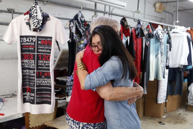 Venezuelan artist and designer Lisu Vega (R) hugs Alexandra Pedrosa (L) in front of her collection "Resistance" in a warehouse in Miami, Florida on June 8, 2017. The models are dressed in scenes of violence in Caracas and handkerchiefs representing the rags used by protesters to protect themselves from police tear gas. It is the "Resistance" collection of Venezuelan fashion designer Lisu Vega. / AFP PHOTO / RHONA WISE