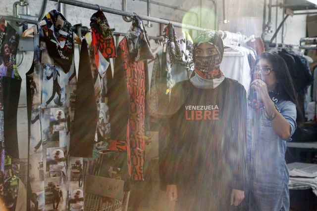 Sunlight streams through a window as Vida Delgato (L) models clothes by Venezuelan artist and designer Lisu Vega (R) from her collection "Resistance" in a warehouse in Miami, Florida on June 8, 2017. The models are dressed in scenes of violence in Caracas and handkerchiefs representing the rags used by protesters to protect themselves from police tear gas. It is the "Resistance" collection of Venezuelan fashion designer Lisu Vega. / AFP PHOTO / RHONA WISE