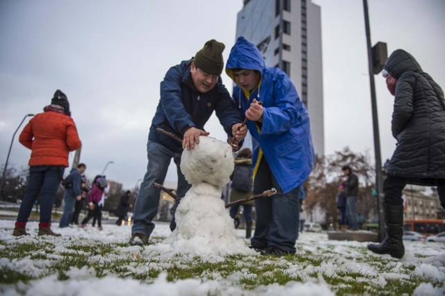 People make a snowman in Santiago on July 15, 2017.  An unusual snowfall --the first of such intensity since 2007-- surprised the inhabitants of the Chilean capital, causing a few power cuts and minor traffic jams, in particular in the eastern areas of the capital, the closest to the Andes mountain range. / AFP PHOTO / Martin BERNETTI