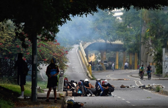 Opposition demonstrators take shelter during an anti-government protest in Caracas, on July 20, 2017. A 24-hour nationwide strike got underway in Venezuela Thursday, in a bid by the opposition to increase pressure on beleaguered leftist President Nicolas Maduro following four months of deadly street demonstrations. / AFP PHOTO / JUAN BARRETO