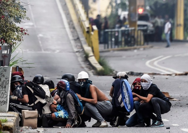 Opposition demonstrators protect themselves from riot police during an anti-government protest in Caracas, on July 20, 2017. A 24-hour nationwide strike got underway in Venezuela Thursday, in a bid by the opposition to increase pressure on beleaguered leftist President Nicolas Maduro following four months of deadly street demonstrations. / AFP PHOTO / JUAN BARRETO