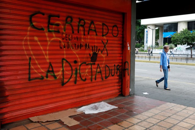 Una mujer camina por una calle cerca de un graffiti que dice "cerrado por la dictadura" durante una huelga convocada para protestar contra el gobierno del presidente venezolano, Nicolás Maduro, en Caracas, Venezuela. 20 julio , 2017. REUTERS/Marco Bello