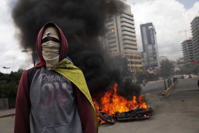 An opposition supporter walks near burning motorcycles as clashes break out while the Constituent Assembly election is being carried out in Caracas, Venezuela, July 30, 2017. REUTERS/Carlos Garcia Rawlins