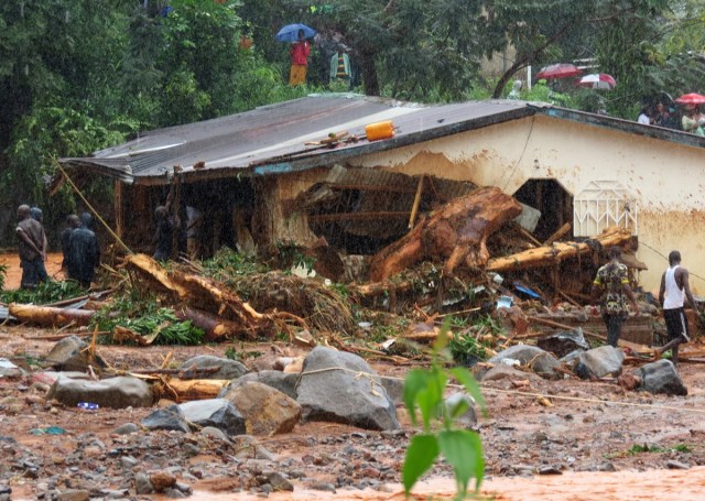 Bystanders and rescue personnel gather beside a flood damaged building in an area of Freetown on August 14, 2017, after landslides struck the capital of the west African state of Sierra Leone. At least 312 people were killed and more than 2,000 left homeless when heavy flooding hit Sierra Leone's capital of Freetown, leaving morgues overflowing and residents desperately searching for loved ones. An AFP journalist at the scene saw bodies being carried away and houses submerged in two areas of the city, where roads turned into churning rivers of mud and corpses were washed up on the streets. / AFP PHOTO / SAIDU BAH