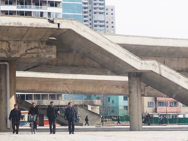 Ciudadanos caminan bajo la carretera de hormigón del Ryugyong, que aparenta estar gravemente dañada en la parte que une las escaleras a la plataforma.