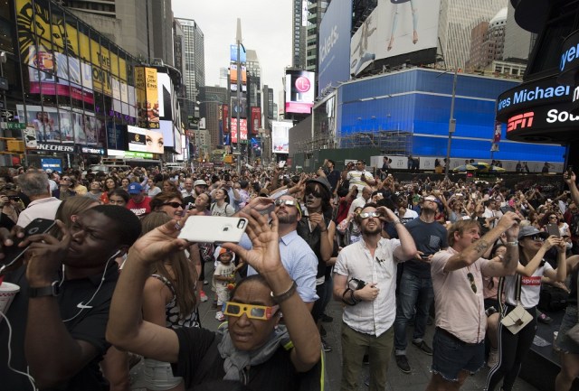 People in Times Square try to takes photos and view the solar eclipse August 21, 2017 in New York. Emotional sky-gazers stood transfixed across North America Monday as the Sun vanished behind the Moon in a rare total eclipse that swept the continent coast-to-coast for the first time in nearly a century. / AFP PHOTO / DON EMMERT