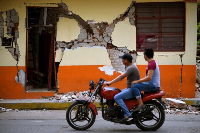 A biker rides in front of a house damaged by the 8.2 magnitude earthquake that hit Mexico's Pacific coast, in Juchitan de Zaragoza, state of Oaxaca on September 8, 2017.  Mexico's most powerful earthquake in a century killed at least 35 people, officials said, after it struck the Pacific coast, wrecking homes and sending families fleeing into the streets. / AFP PHOTO / PEDRO PARDO