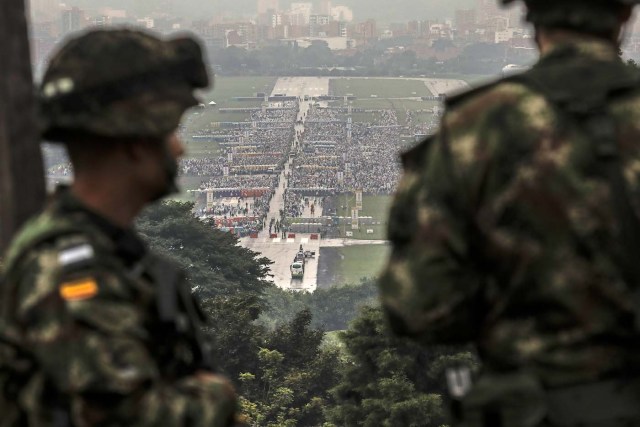 Soldiers keep watch from the distance as people gather at the Enrique Olaya Herrera airport in Medellin, Colombia, for a mass to be officiated by Pope Francis on September 9, 2017. Pope Francis visits the Colombian city of Medellin, former stronghold of the late drug baron Pablo Escobar, on the fourth day of a papal tour to promote peace. / AFP PHOTO / Joaquin SARMIENTO