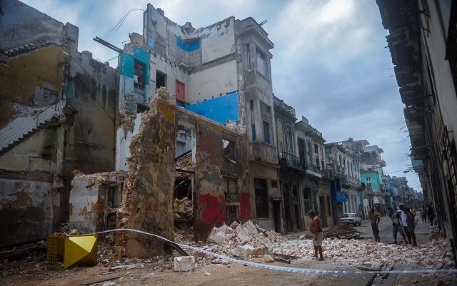 Cubans stand bt a collapsed building in Havana, on September 9, 2017.  Irma's blast through the Cuban coastline weakened the storm to a Category Three, but it is still packing 125 mile-an-hour winds (205 kilometer per hour) and was expected to regain power before hitting the Florida Keys early Sunday, US forecasters said. The Cuban government extended its maximum state of alert to three additional provinces, including Havana, amid fears of flooding in low-lying areas. / AFP PHOTO / YAMIL LAGE