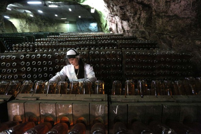 An employee turns bottles in the "Artwinery" winery firm in the eastern Ukrainian city of Bakhmut on July 12, 2017. The winery is located in a government-held town just two dozen kilometres (15 miles) from the frontline in Ukraine's low-level war, where the army and Russian-backed rebels continue to lob deadly artillery barrages at each other. The town spent around a month under rebel control in 2014, and in 2015 the frontline was so close that the town came under rebel shelling. But despite more than three years of fighting that has claimed some 10,000 lives, Nasyrov's employer, Artwinery, has never stopped production. / AFP PHOTO / Aleksey FILIPPOV