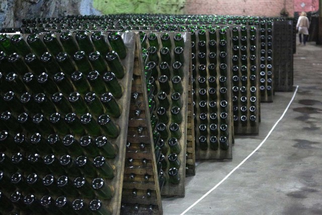 An employee works past bottles of wine in the "Artwinery" winery firm in the eastern Ukrainian city of Bakhmut on July 12, 2017. The winery is located in a government-held town just two dozen kilometres (15 miles) from the frontline in Ukraine's low-level war, where the army and Russian-backed rebels continue to lob deadly artillery barrages at each other. The town spent around a month under rebel control in 2014, and in 2015 the frontline was so close that the town came under rebel shelling. But despite more than three years of fighting that has claimed some 10,000 lives, Nasyrov's employer, Artwinery, has never stopped production. / AFP PHOTO / Aleksey FILIPPOV