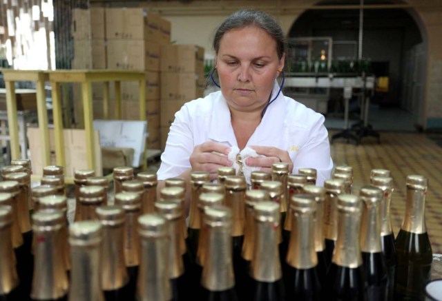 An employee checks bottles as she works on the production line in the "Artwinery" winery firm in the eastern Ukrainian city of Bakhmut on July 12, 2017. The winery is located in a government-held town just two dozen kilometres (15 miles) from the frontline in Ukraine's low-level war, where the army and Russian-backed rebels continue to lob deadly artillery barrages at each other. The town spent around a month under rebel control in 2014, and in 2015 the frontline was so close that the town came under rebel shelling. But despite more than three years of fighting that has claimed some 10,000 lives, Nasyrov's employer, Artwinery, has never stopped production. / AFP PHOTO / Aleksey FILIPPOV