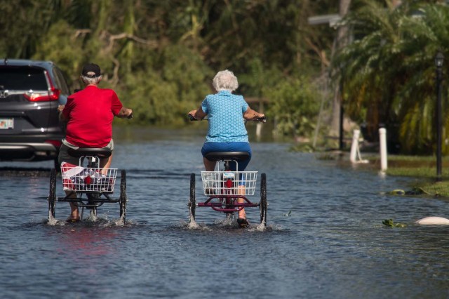 Two retirees ride tricycles through a flooded street at the Enchanted Shores manufactured home park in Naples, Florida, on September 11, 2017 after Hurricane Irma hit Florida. / AFP PHOTO / NICHOLAS KAMM
