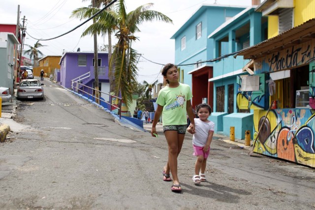 Two girls walk on a street in the neighbourhood of La Perla in the aftermath of Hurricane Maria in San Juan, Puerto Rico, on September 22, 2017. Puerto Rico battled dangerous floods Friday after Hurricane Maria ravaged the island, as rescuers raced against time to reach residents trapped in their homes and the death toll climbed to 33. / AFP PHOTO / Ricardo ARDUENGO