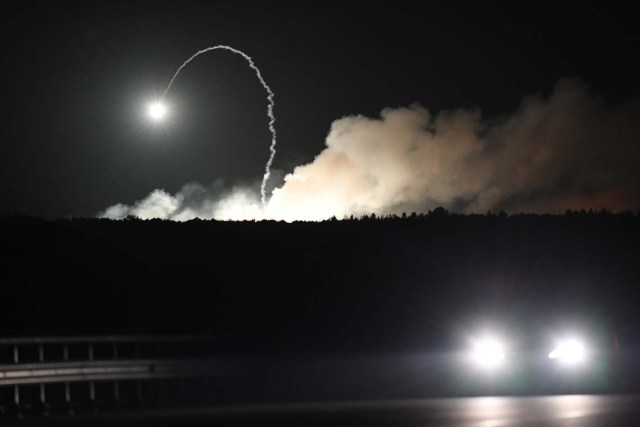 A car passes while munitions explode at a military depot on September 27, 2017 near Kalynivka. Ukranian authorities evacuated nearly 30,000 people September 27 from the central Vinnytsya region after a huge munitions depot caught fire and set off artillery shells and blasts prosecutors were treating as an act of "sabotage". It was the second major incident affecting a Ukrainian weapons storage site this year. Kiev blamed the first one in March on Moscow and its Russian-backed insurgents fighting Ukrainian forces in the war-wrecked east -- a charge both sides denied. / AFP PHOTO / Sergei SUPINSKY