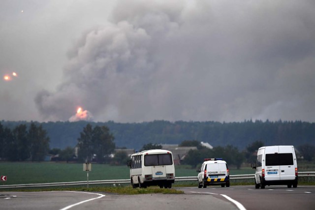 Cars pass as munitions explode at a military depot on September 27, 2017 near Kalynivka. Ukranian authorities evacuated nearly 30,000 people September 27 from the central Vinnytsya region after a huge munitions depot caught fire and set off artillery shells and blasts prosecutors were treating as an act of "sabotage". It was the second major incident affecting a Ukrainian weapons storage site this year. Kiev blamed the first one in March on Moscow and its Russian-backed insurgents fighting Ukrainian forces in the war-wrecked east -- a charge both sides denied. / AFP PHOTO / Sergei SUPINSKY