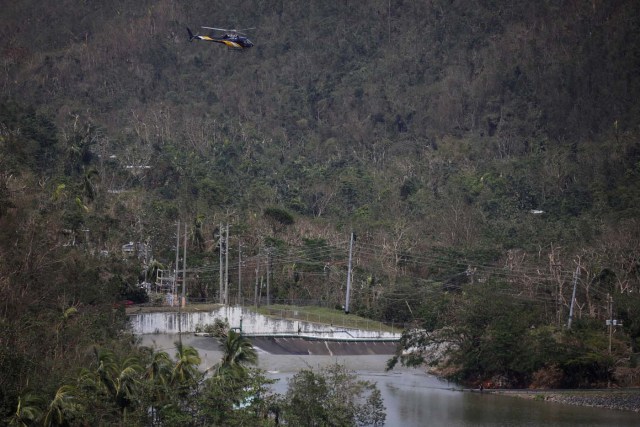 People look at water flowing over the road as a helicopter flies over them at the dam of the Guajataca lake after the area was hit by Hurricane Maria in Guajataca, Puerto Rico September 23, 2017. REUTERS/Carlos Garcia Rawlins