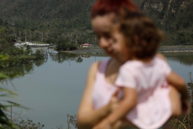 Yadira Nieves carries her daughter as they look at water flowing over the road at the dam of the Guajataca lake after the area was hit by Hurricane Maria in Guajataca, Puerto Rico September 23, 2017. REUTERS/Carlos Garcia Rawlins