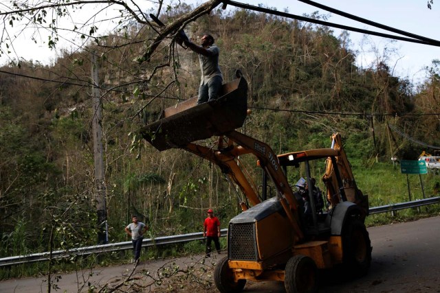 A worker standing on a backhoe loader uses a chainsaw to remove fallen trees from the street after the area was hit by Hurricane Maria in Camuy, Puerto Rico September 23, 2017. REUTERS/Carlos Garcia Rawlins