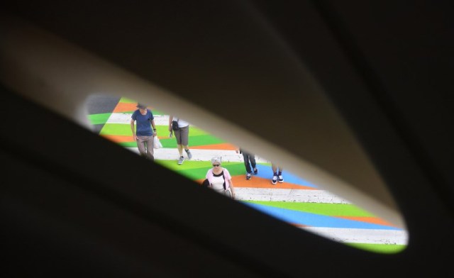 Pedestrians cross a painted crosswalk by Venezuelan-born artist Carlos Cruz-Diez, as seen through windows inside the Broad Museum in Los Angeles, California on September 14, 2017,  where the painted crosswalks are a part of the Pacific Standard Time LA/LA Show, an exploration of Latino and Latin American Art in dialogue with Los Angeles.   / AFP PHOTO / FREDERIC J. BROWN