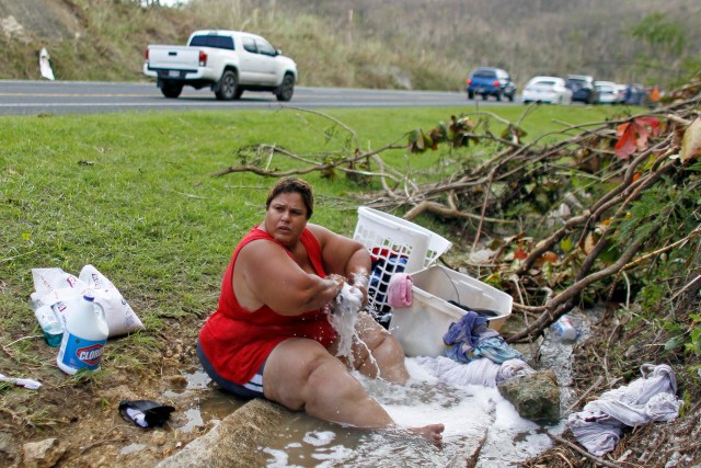 Iris Vazquez washes clothing at an open road drainage next to a road in Corozal, west of San Juan, Puerto Rico, on September 24, 2017 following the passage of Hurricane Maria. / AFP PHOTO / Ricardo ARDUENGO