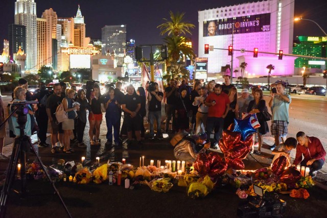 People gather and light candles at a makeshift memorial near the Mandalay Hotel on the Las Vegas Strip, in Las Vegas, Nevada on October 3, 2017, after a gunman killed 58 people and wounded more than 500 others, before taking his own life, when he opened fire from a hotel on a country music festival. Police said the gunman, a 64-year-old local resident named as Stephen Paddock, had been killed after a SWAT team responded to reports of multiple gunfire from the 32nd floor of the Mandalay Bay, a hotel-casino next to the concert venue. / AFP PHOTO / Robyn Beck