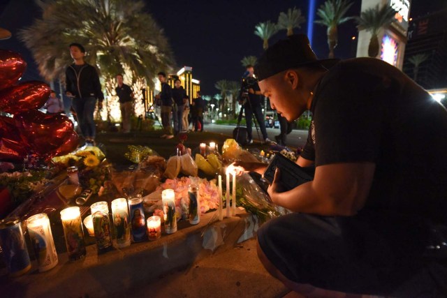 Edrian Pateno of Corona, California lights candles at a makeshift memorial near the Mandalay Hotel on the Las Vegas Strip, in Las Vegas, Nevada on October 3, 2017, after a gunman killed 58 people and wounded more than 500 others, before taking his own life, when he opened fire from a hotel on a country music festival. Police said the gunman, a 64-year-old local resident named as Stephen Paddock, had been killed after a SWAT team responded to reports of multiple gunfire from the 32nd floor of the Mandalay Bay, a hotel-casino next to the concert venue. / AFP PHOTO / Robyn Beck